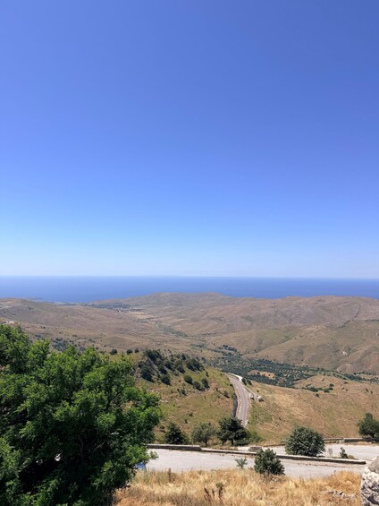 A winding road through a hilly landscape with a clear blue sky and the ocean in the distance. 5