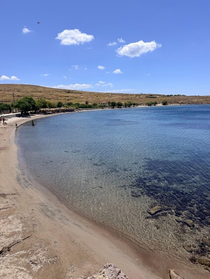 A clear blue lake with a sandy beach, a few people near the water, and a hilly landscape in the background. 2