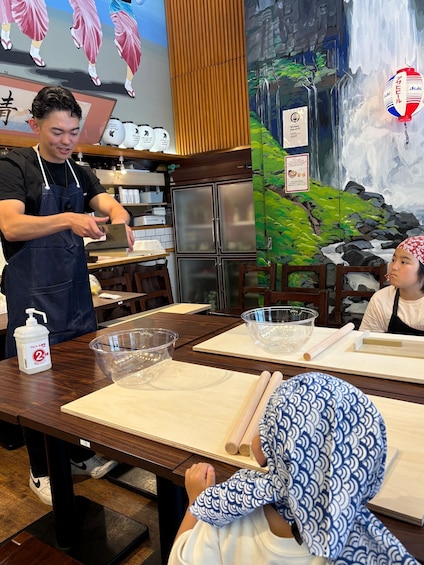 A person cutting food on a wooden table in a restaurant with a mural of a waterfall. 4