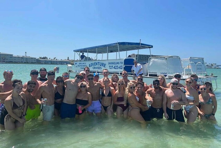 A group of people in shallow water near a boat with a blue canopy, a clear sky, and a calm sea. 5