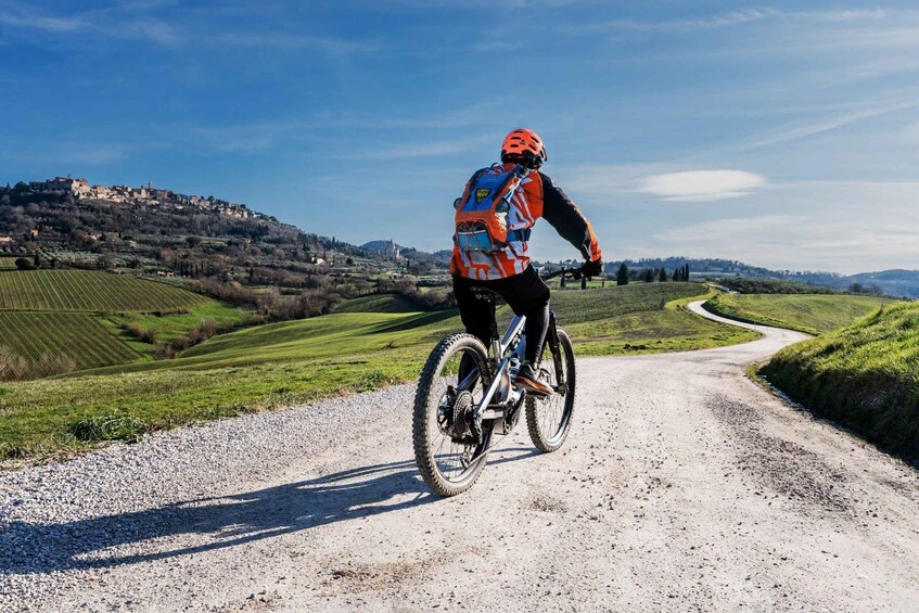 A cyclist on a gravel road with a hilly landscape and a distant village. 1
