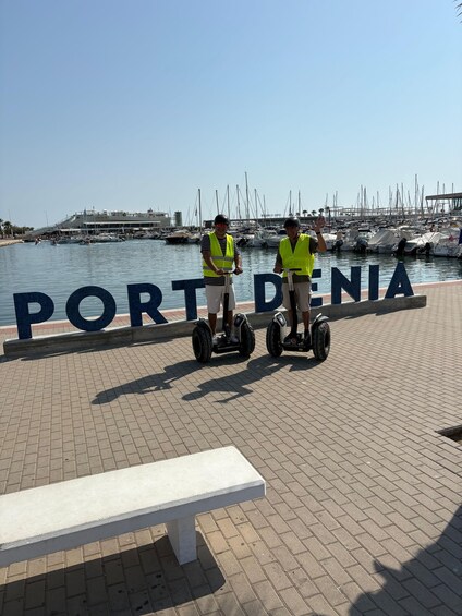 Two people on Segways in front of a marina with boats and the text 'PORT DENIA'. 2