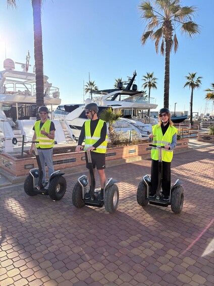 Three people on segways near a marina with boats and palm trees. 3