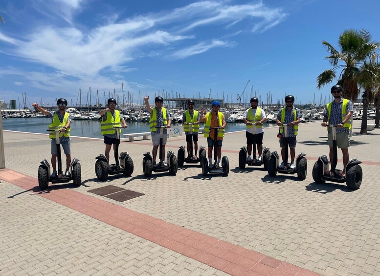 A group of people on segways near a marina with boats. 1