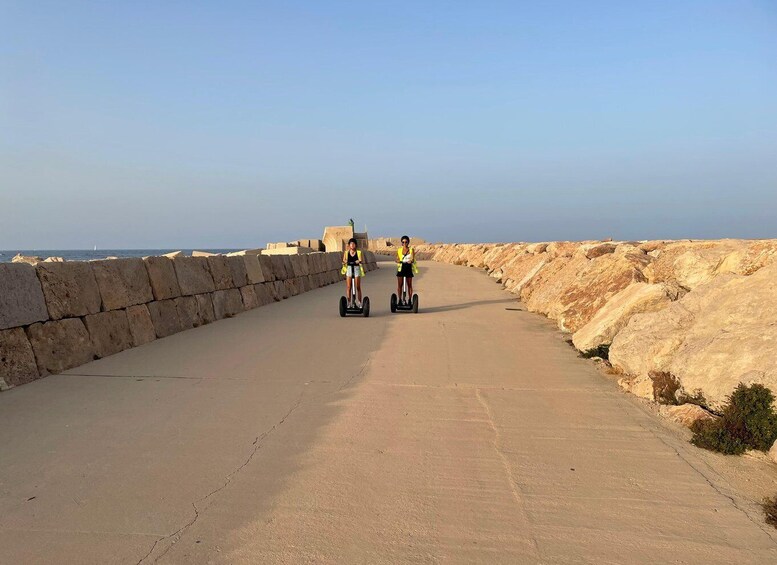 Two people on segways on a paved path beside a rocky coastline. 4