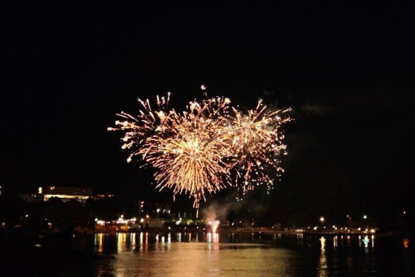 A nighttime fireworks display over a body of water with reflections of lights on the surface. 2