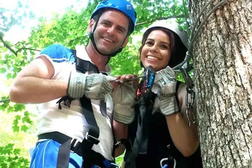 Two people in helmets and harnesses, preparing for a zip-lining activity. 2