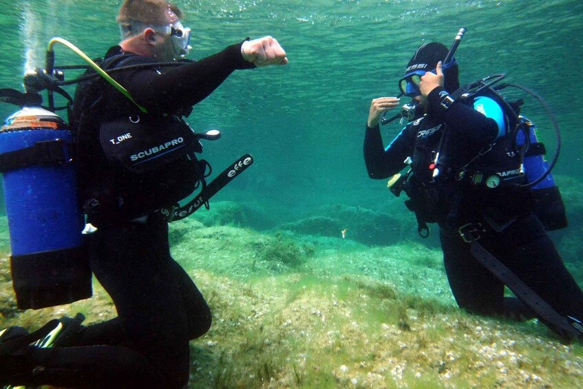 Two scuba divers underwater, one pointing and the other adjusting equipment. 2