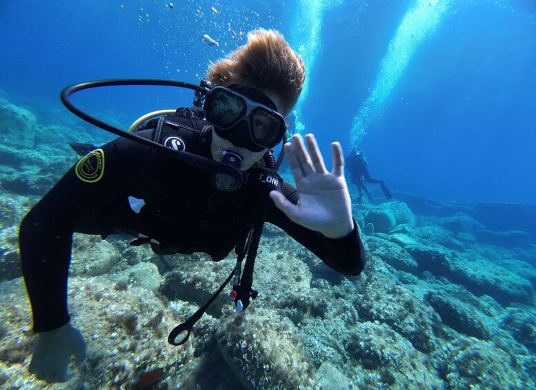 A diver underwater with a hand gesture, surrounded by coral and marine life. 1
