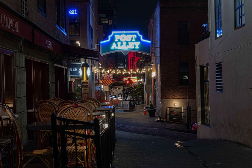 A nighttime street scene with a neon sign for 'POST ALLEY,' wicker furniture, and brick buildings. 2