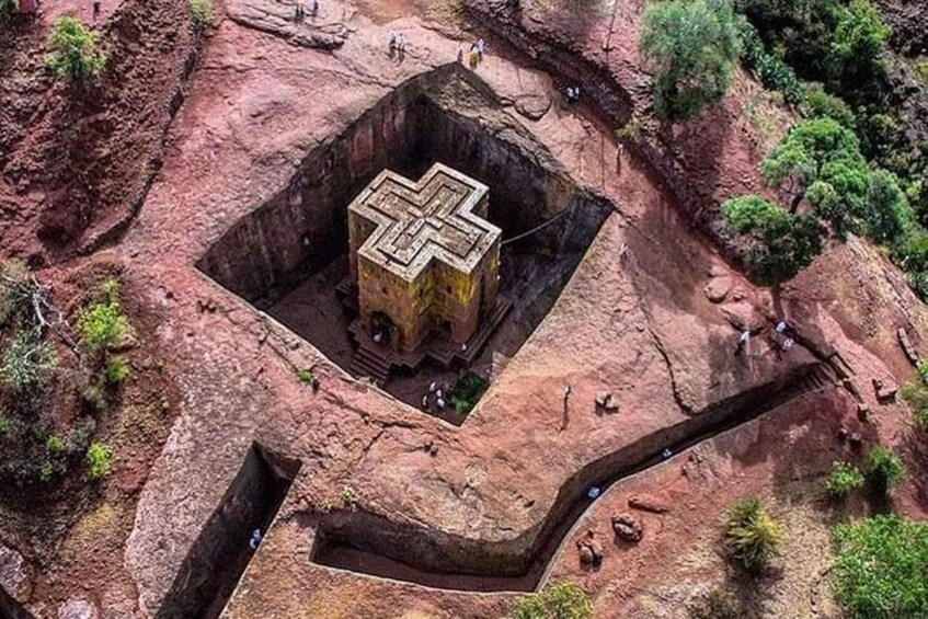 An aerial view of a large, square-shaped ancient structure with a cross-like design, surrounded by red rock formations and sparse vegetation. 2