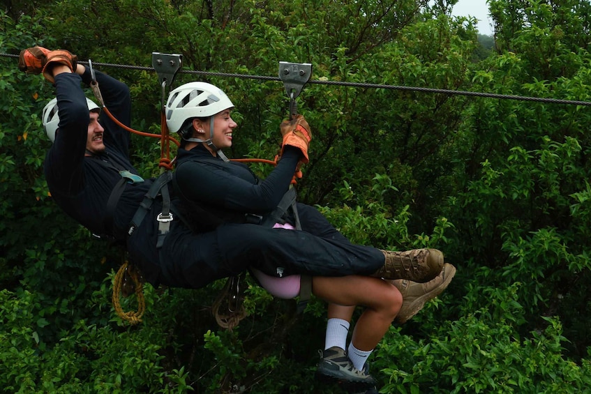 Two people zip-lining through a forested area. 2