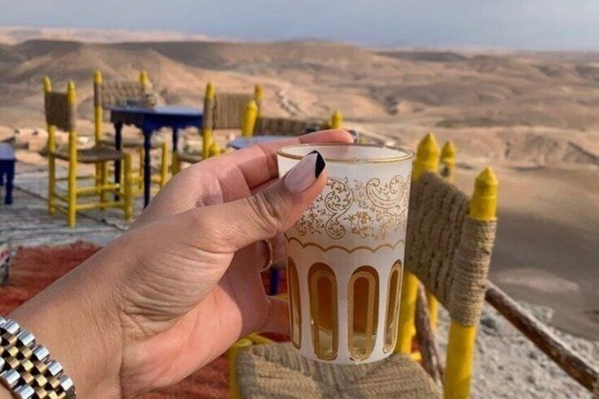 A hand holding a patterned glass with a desert landscape in the background. 5