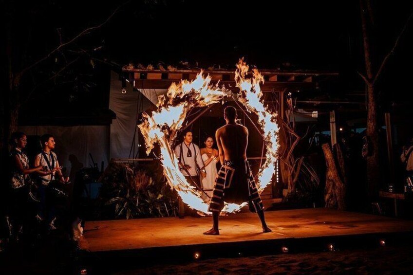 A performer with a fire hoop, audience watching, and a stage with trees in the background. 4