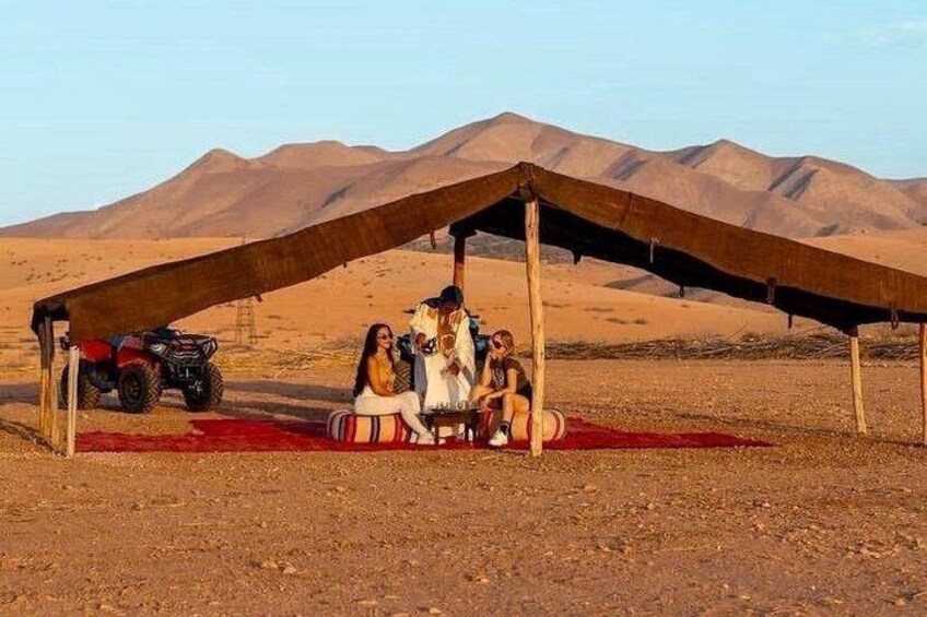 A group of people under a tent in a desert with mountains in the background. 2