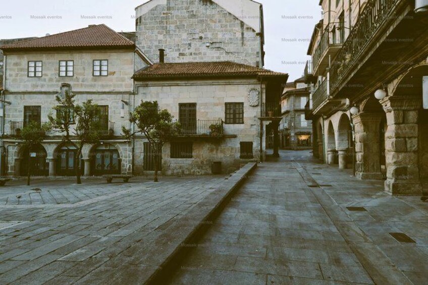 A historic stone square with buildings, a narrow water channel, and traditional architecture. 2