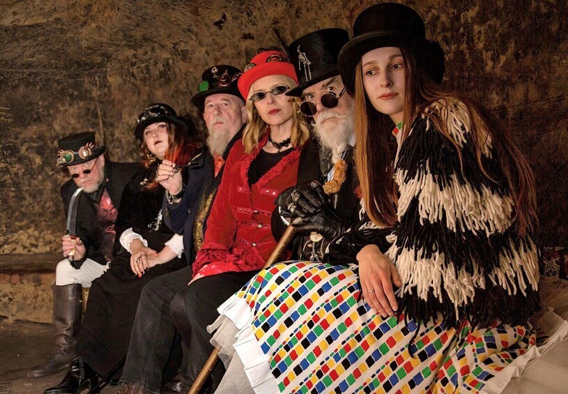 A group of people in historical costumes seated in a stone-walled room. 5