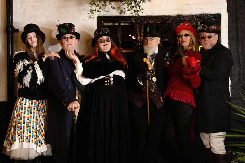 A group of people in historical costumes standing in front of a rustic door. 3