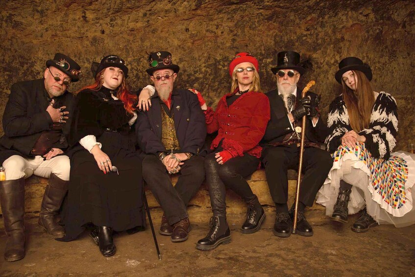 A group of people dressed in historical costumes sitting on a stone wall. 1