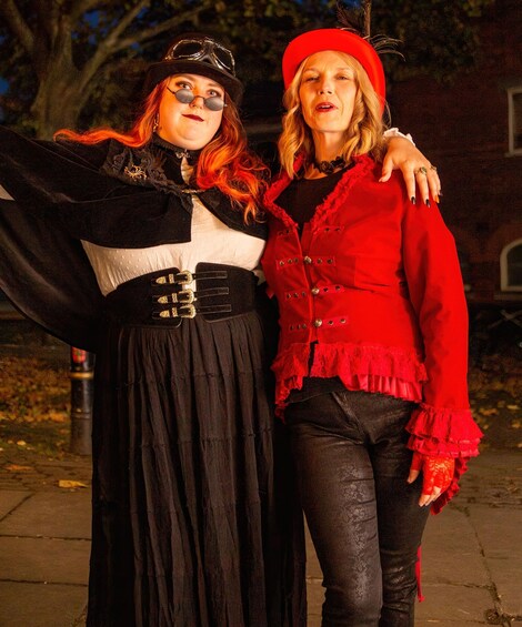 Two people in period costumes, one in black and white, the other in red, standing on a sidewalk at night. 2