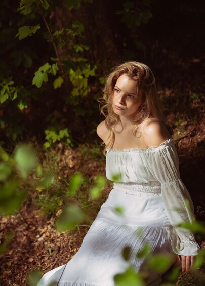 A person in a white dress sitting in a forest. 4