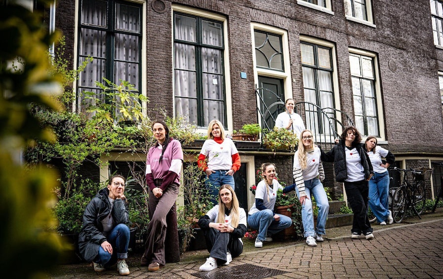 A group of people standing and sitting in front of a brick building with large windows and potted plants. 1