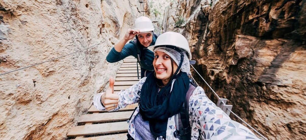 Two people on a wooden bridge in a canyon with rocky walls. 4