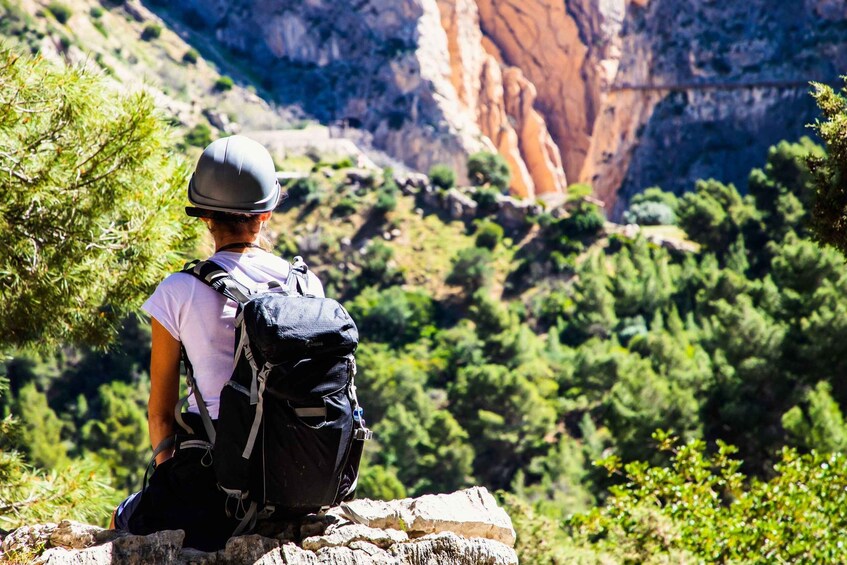 A person sitting on a rock with a backpack, overlooking a mountainous landscape with greenery and cliffs. 1