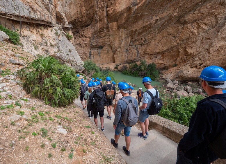 A group of people in hard hats walking along a path beside a canyon with a river. 3