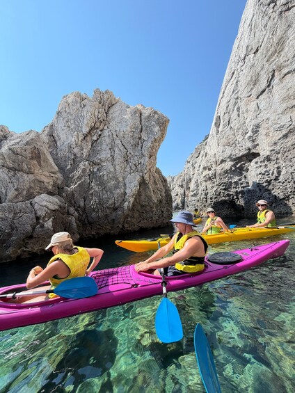 People kayaking in clear water with rocky cliffs in the background. 3