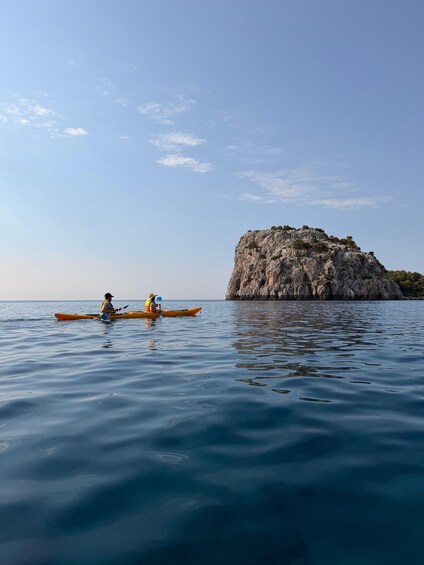 Two people kayaking on calm water with a rocky island in the background. 1
