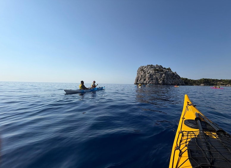 Two people kayaking on calm waters, a rocky island in the background, and a yellow kayak in the foreground. 5