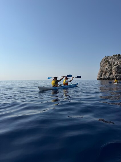 Two people kayaking on calm water near a rocky cliff. 5