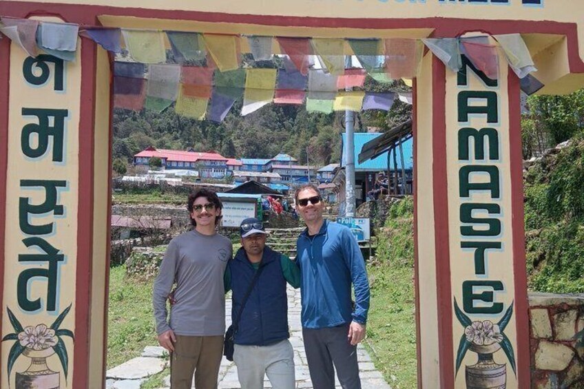 A group of people standing in front of a sign with 'RAMASTE' written on it, with a mountainous landscape in the background. 5