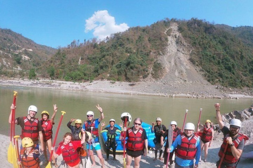 A group of people in life jackets and helmets by a river, some holding paddles. 3