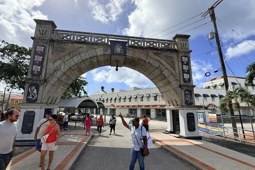 A stone archway with inscriptions, a pedestrian crossing, and a building in the background. 1