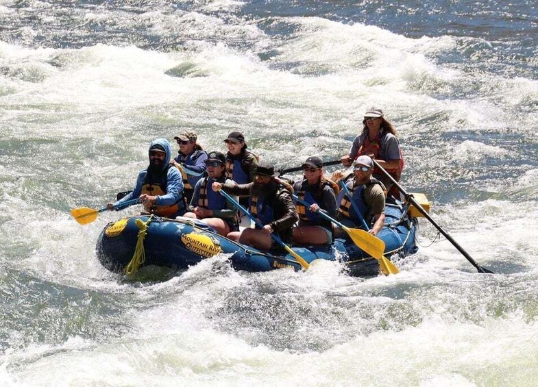 A group of people in a blue inflatable raft navigating through white water rapids. 1