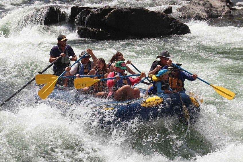 A group of people in a blue inflatable raft navigating through a river with rapids. 3