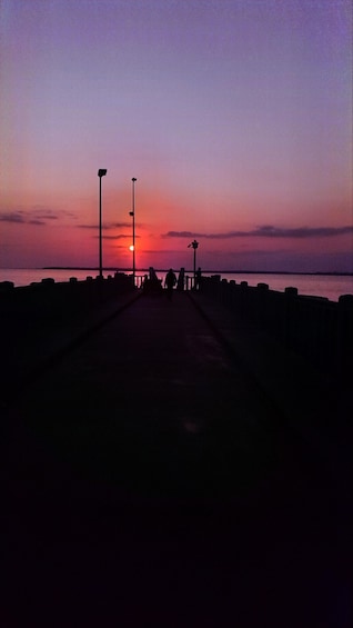 A sunset over a pier with silhouettes of people and street lamps. 1