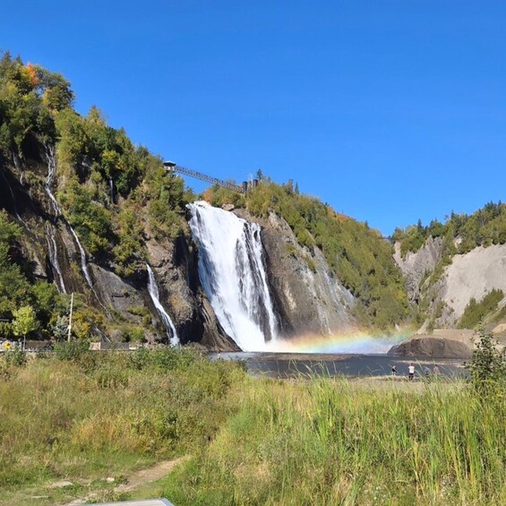 A waterfall cascading down a rocky cliff, surrounded by lush greenery and a clear blue sky. 2