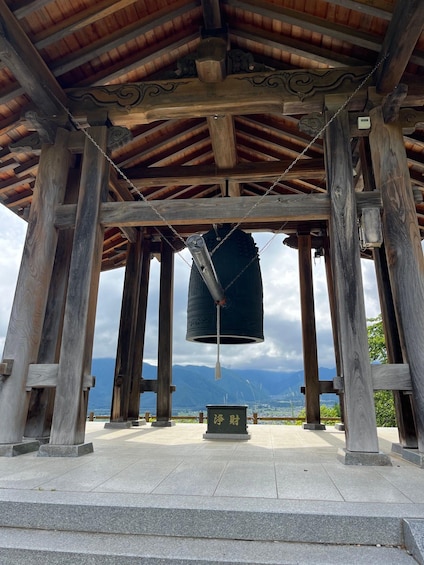 A traditional wooden bell tower with a bell hanging from a chain, set against a mountainous backdrop. 4