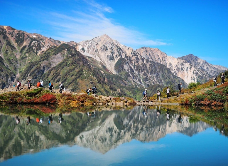 Hikers on a mountain trail with a lake reflecting the surrounding landscape. 1