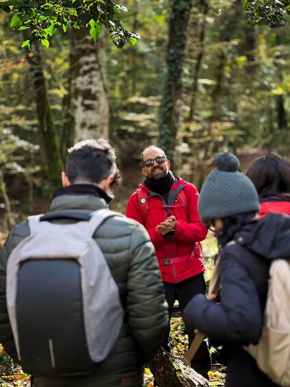 A group of people in a forested area, one person in a red jacket appears to be leading the group. 2