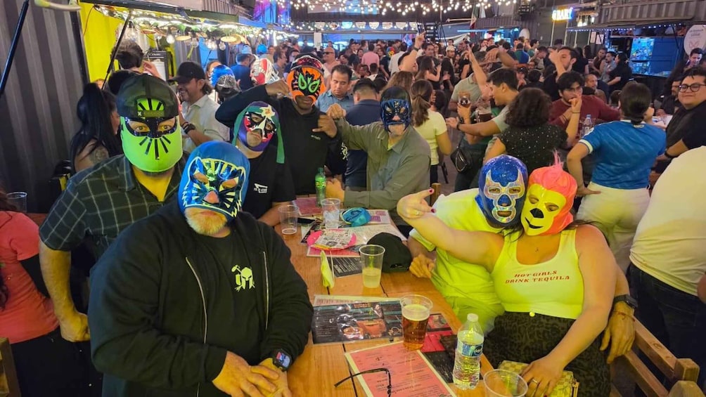 A crowded indoor event with people wearing colorful masks and holding drinks. 2