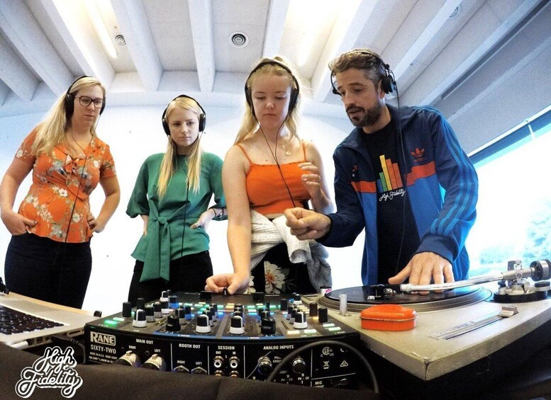 Four people in a room with a DJ setup, including a RANE mixer and a laptop. 1