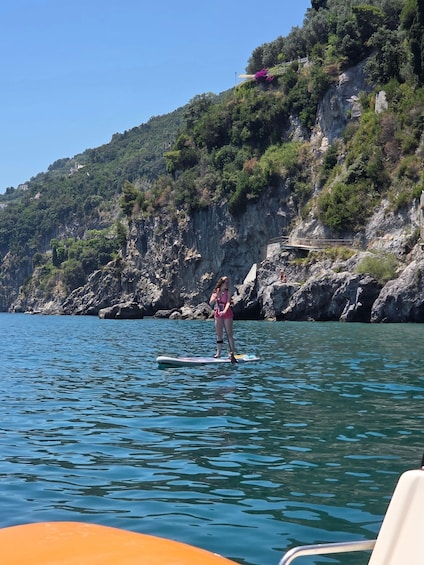 A person paddleboarding on calm waters with a mountainous coastline in the background. 2