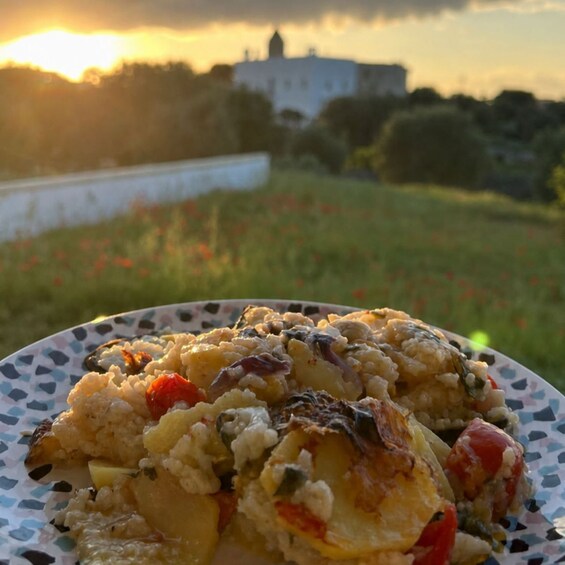 A plate of food with vegetables and grains, set against a sunset with a building in the background. 2