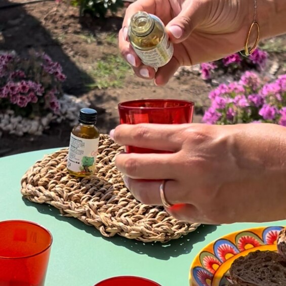 A hand pouring a liquid from a small bottle onto a red cup on a woven mat. 4