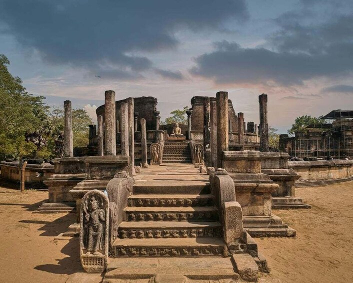 Ancient stone ruins with a central staircase leading to a structure, surrounded by columns and statues. 1