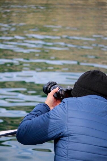 A person taking a photograph with a camera by a body of water. 4